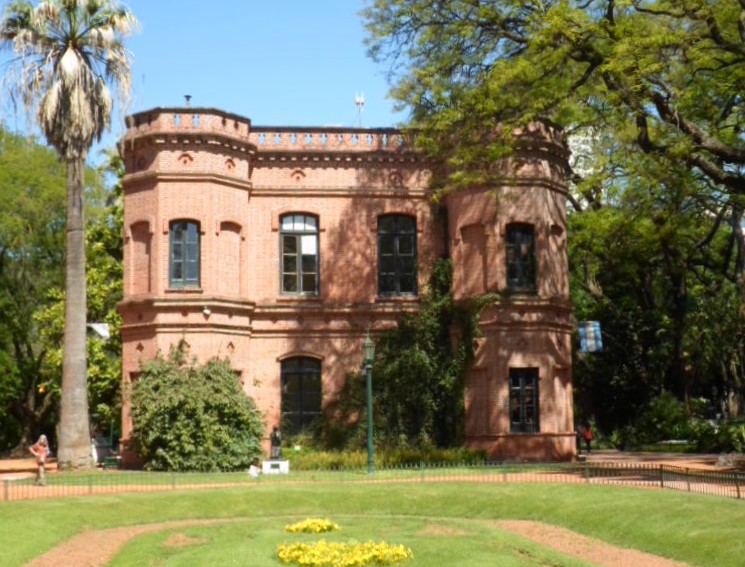 La imagen muestra una foto del Jardín Botánico donde se ve un jardín y un edificio diseñados por Carlos Thays