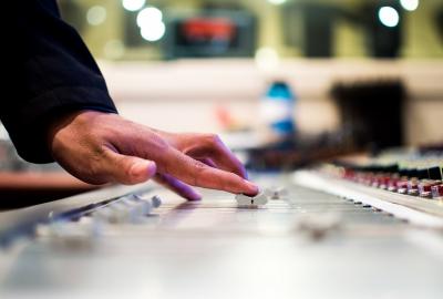 La imagen muestra una consola de sonido y una mano que la está operando