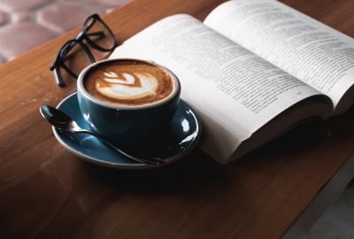 En la imagen se ve una taza de café con libro sobre mesa