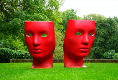En la imagen se ve un jardín con dos esculturas que representan la comedia y la tragedia en el teatro. Son máscaras grandes y de color rojo.