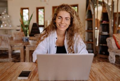La imagen muestra a una mujer sonriendo frente a una computadora en situación de conversación
