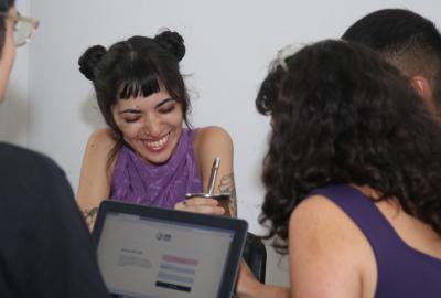 La imagen muestra  a estudiantes dentro de un aula, charlando y sonriendo