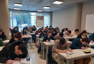 La imagen muestra un aula con estudiantes extranjeros realizando el examen escrito CEA