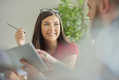 La imagen muestra a una mujer sonriente conversando con un compañero