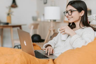 La imagen muestra a una mujer mirando la computadora y sonriendo, tiene una taza de café en la mano